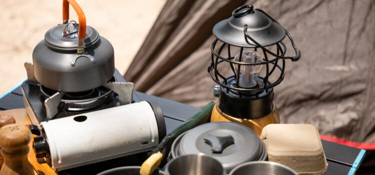 Cooking gear for a tranquil beach campsite, kettle, pot, pan, gas stove, flashlight, and camera set on a table by the tent. Enjoy a serene camping experience amidst nature.
