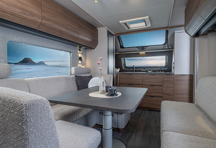 Knaus Nordwind caravan interior with dining table, grey upholstered seating and kitchenette by large windows