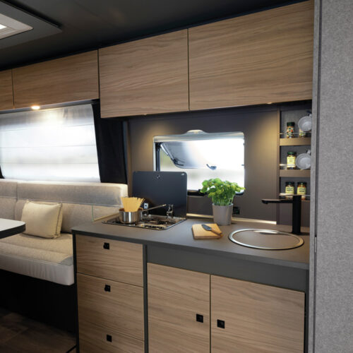 Compact kitchen with wooden cabinets, gas hob and sink in the Dethleffs Trend I 7027 caravan interior.