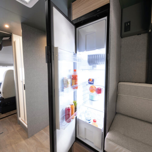 Open fridge with drinks and fruit in the Dethleffs Trend I 7027 motorhome kitchen area