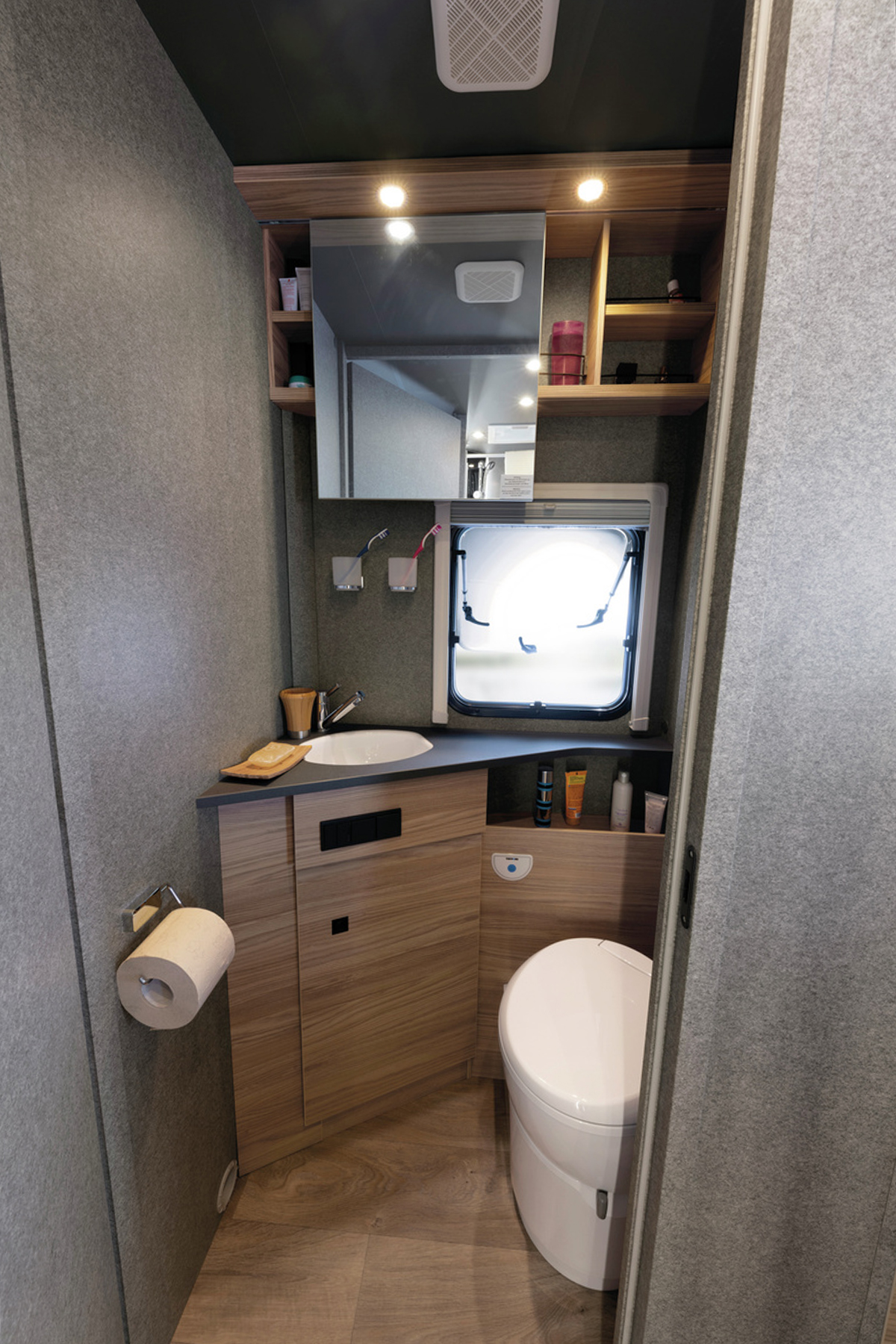 Compact washroom in the Dethleffs Trend I 7027 with toilet, corner sink, mirrored cabinet and roof vent.