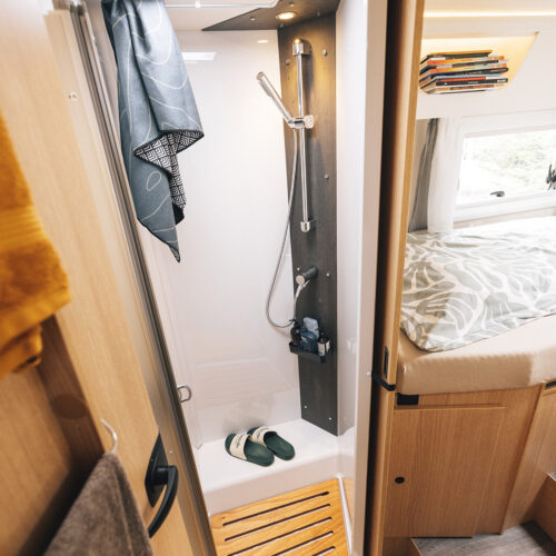 Compact shower cubicle in the Sunlight UNLTD T 7433 S motorhome, with wooden duckboard and bedroom visible beyond.