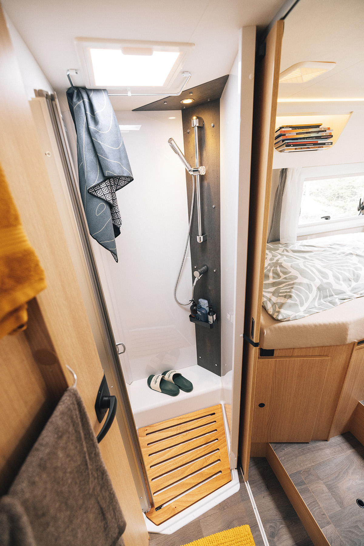 Compact shower cubicle in the Sunlight UNLTD T 7433 S motorhome, with wooden duckboard and bedroom visible beyond.