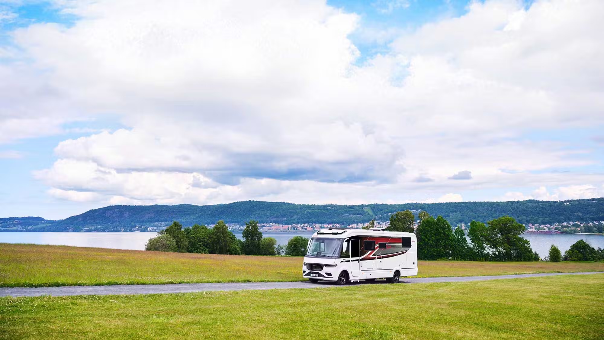 Kabe Imperial 4x4 motorhome parked on a lakeside road with rolling hills and grassy meadow in the background