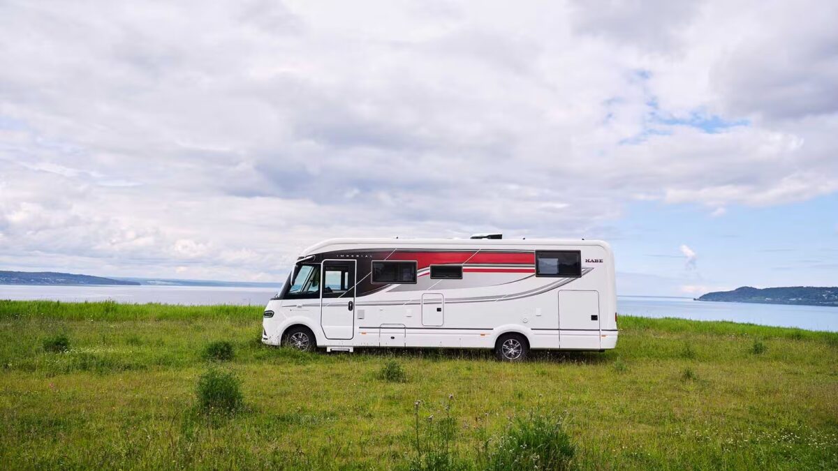 Kabe Imperial 4x4 motorhome parked on grass beside a lake, showcasing red and grey exterior stripe design.