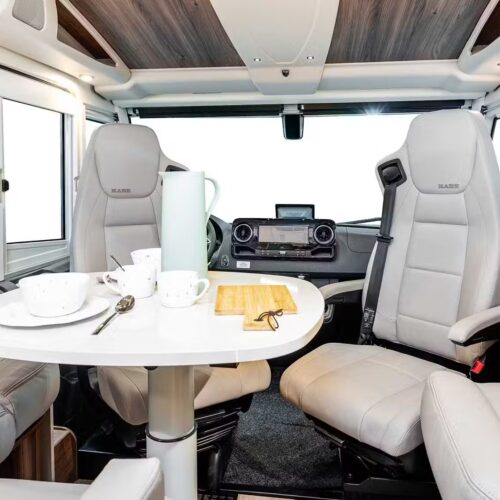 Kabe Imperial 4x4 motorhome interior showing swivel cab seats, dinette table with crockery, and dashboard