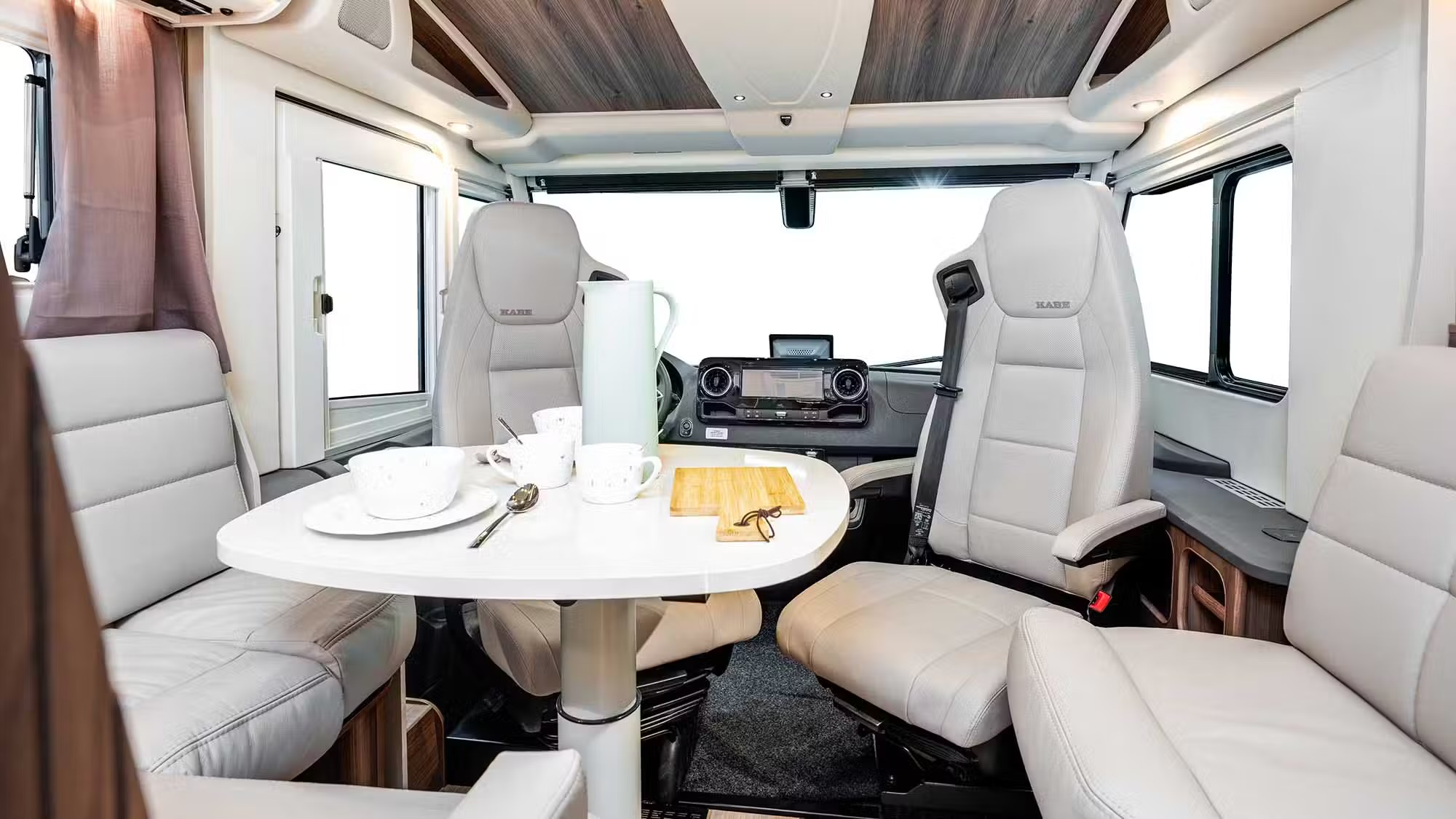 Kabe Imperial 4x4 motorhome interior showing swivel cab seats, dinette table with crockery, and dashboard