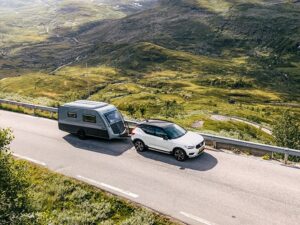 Kip Kompakt caravan towed by white Volvo SUV on mountain road through scenic Norwegian valley