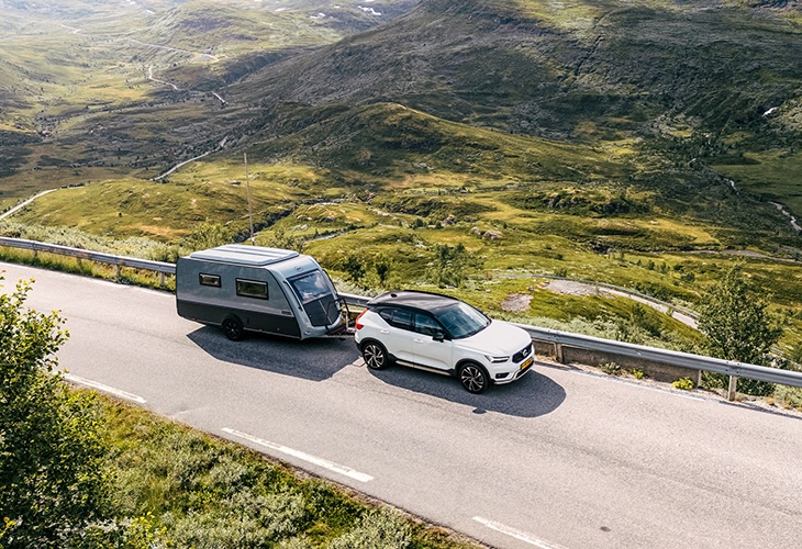 Kip Kompakt caravan towed by white Volvo SUV on mountain road through scenic Norwegian valley
