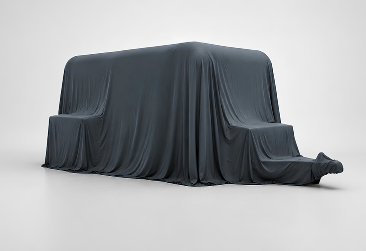 Dark grey fabric cover draped over new Lume caravan model, concealing its shape ahead of official reveal.
