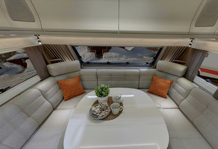 Kabe Royal 600 TDL caravan interior with U-shaped lounge seating, oval table and snowy mountain view through window.