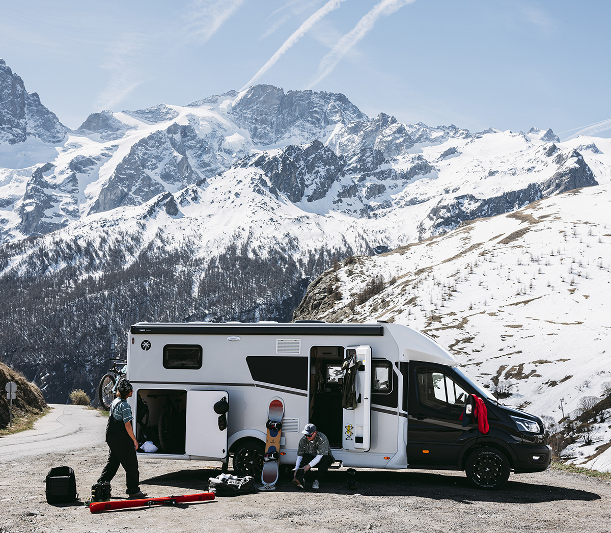 Sunlight UNLTD motorhome parked in snowy Alps with two people unpacking ski and snowboard gear, mountains behind.