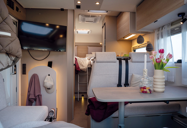LMC Tracer 690 EL 2027 camper interior with lounge seating, wall-mounted TV and rear bunk beds visible