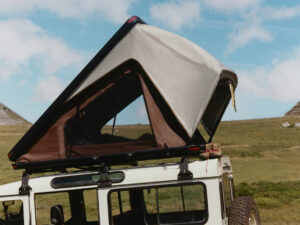 Zara Home rooftop tent open on white Land Rover Defender, set against grassy hills and blue sky