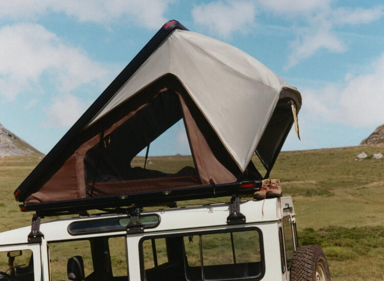 Zara Home rooftop tent open on white Land Rover Defender, set against grassy hills and blue sky