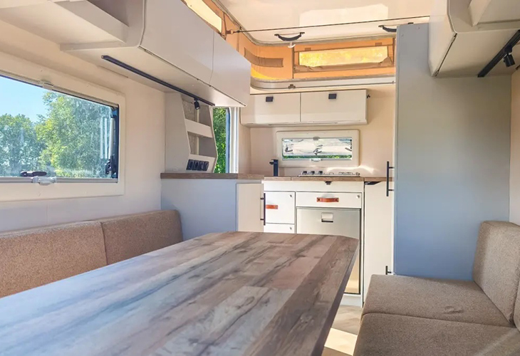 Kip Kompakt caravan interior with wooden dining table, cushioned seating and compact white kitchen units