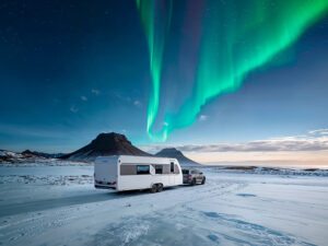Knaus Nordwind caravan towed by SUV on snowy terrain under the northern lights, with mountains in the background.
