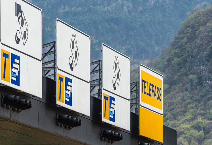 Brenner Autobahn toll booths A22 with overhead signs and Telepass lane, forested mountains behind