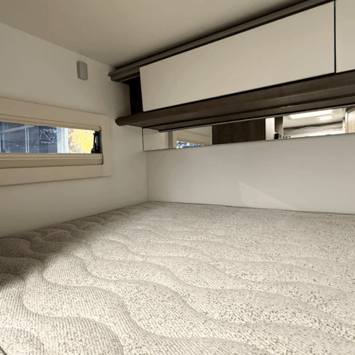 Benimar Kaleo K640 motorhome overhead bed with mattress, small window and mirrored storage cupboards above.