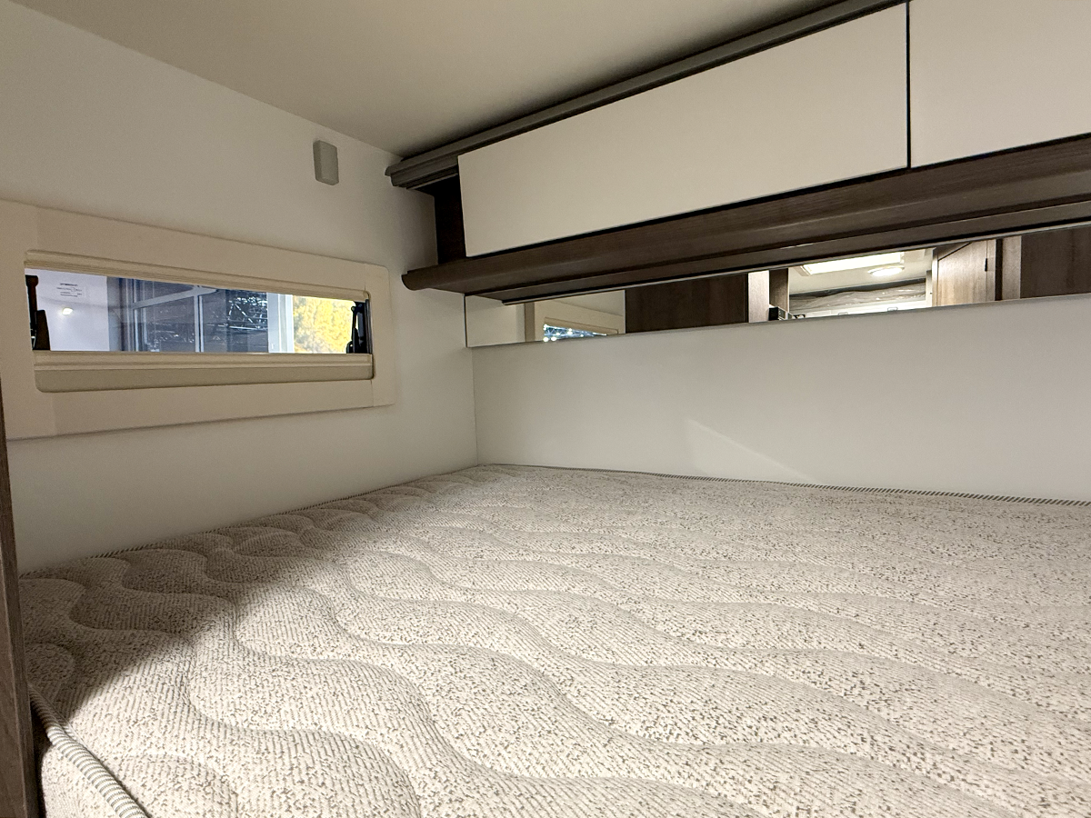 Benimar Kaleo K640 motorhome overhead bed with mattress, small window and mirrored storage cupboards above.