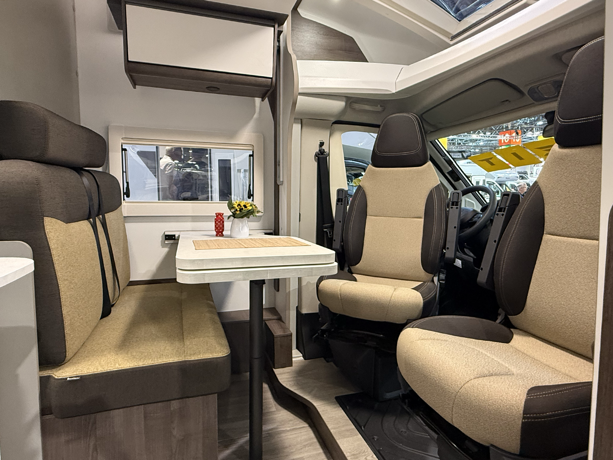 Benimar Kaleo K640 motorhome interior with dinette seating, table and swivel cab seats in beige and brown upholstery.