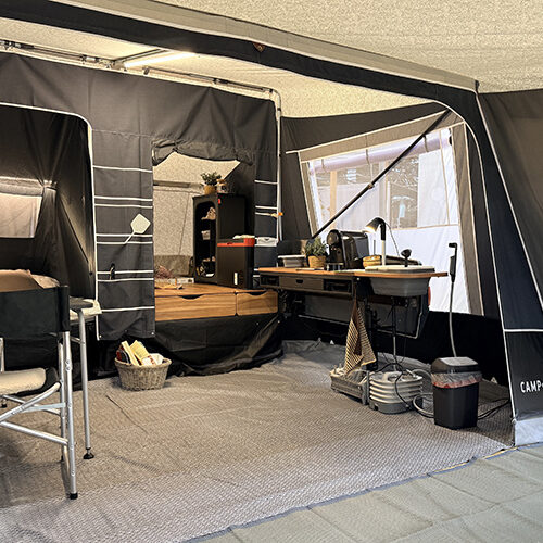 Interior of the Camp-let Alba tent trailer showing canvas awning, camp chair, desk area and storage drawers.
