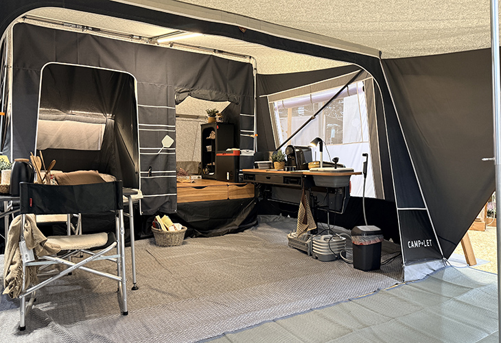 Interior of the Camp-let Alba tent trailer showing canvas awning, camp chair, desk area and storage drawers.