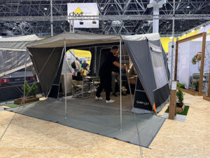 Camp-let Alba tent trailer set up at trade show with awning, groundsheet and two people inside