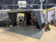 Camp-let Alba tent trailer set up at trade show with awning, groundsheet and two people inside