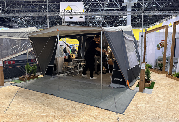 Camp-let Alba tent trailer set up at trade show with awning, groundsheet and two people inside