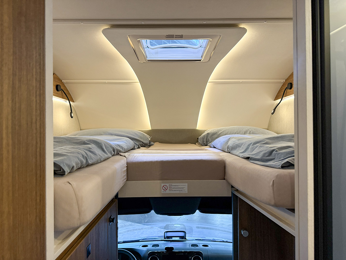 Dethleffs Graneo alcove bed above cab with skylight, reading lights and grey bedding over dashboard