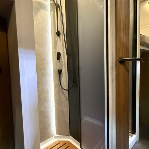 Compact shower cubicle with sliding glass door and teak floor in the Dethleffs Graneo motorhome bathroom.