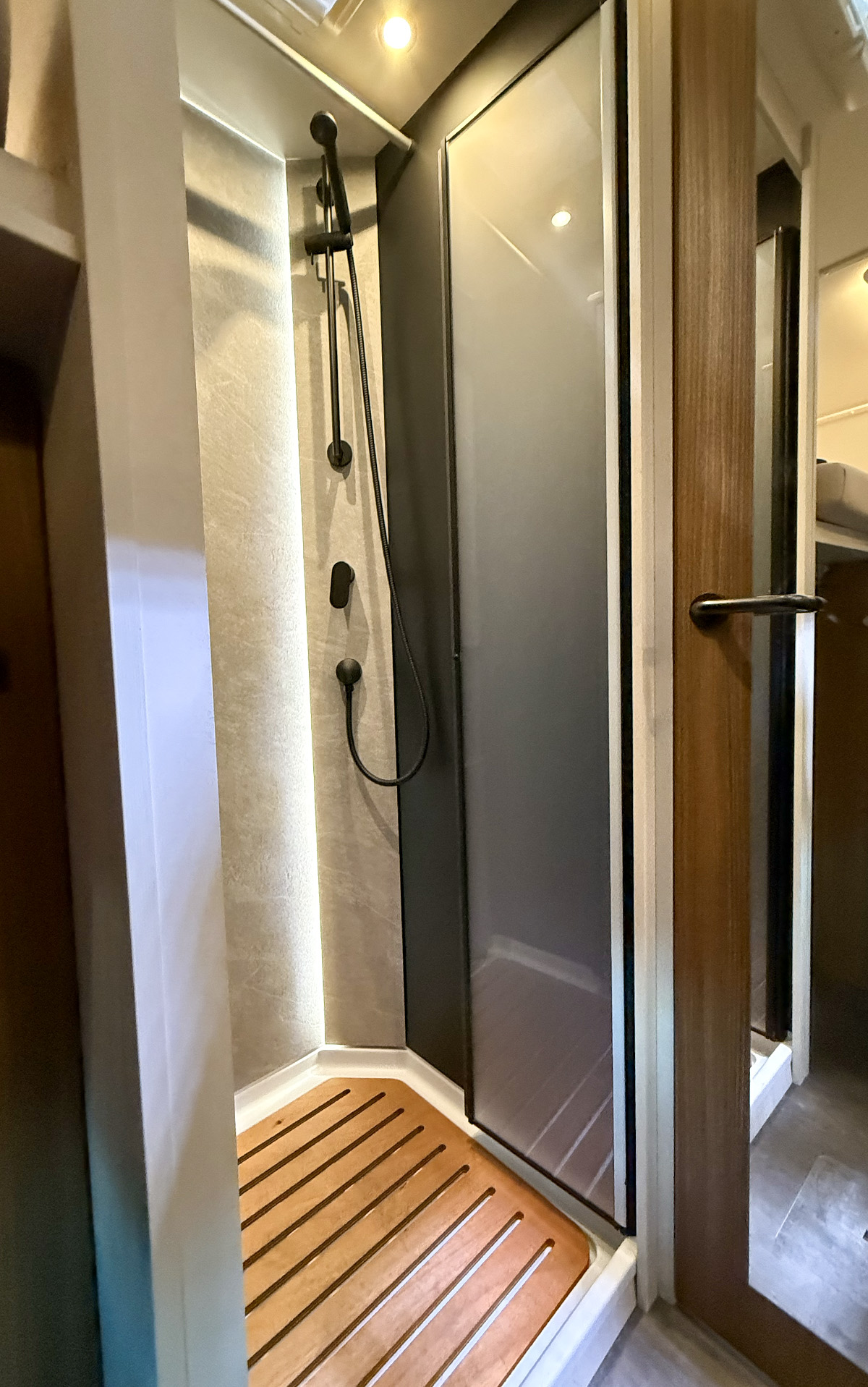 Compact shower cubicle with sliding glass door and teak floor in the Dethleffs Graneo motorhome bathroom.