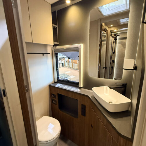 Compact bathroom in the Dethleffs Graneo motorhome with toilet, vessel sink, mirror and shower behind glass door.