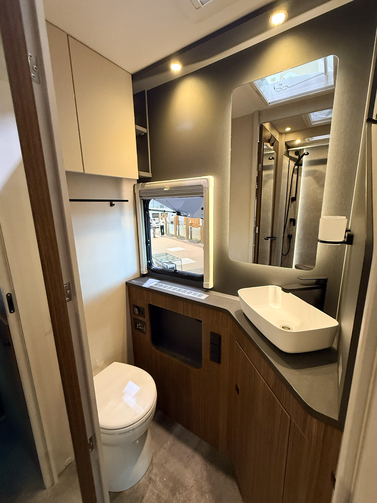 Compact bathroom in the Dethleffs Graneo motorhome with toilet, vessel sink, mirror and shower behind glass door.