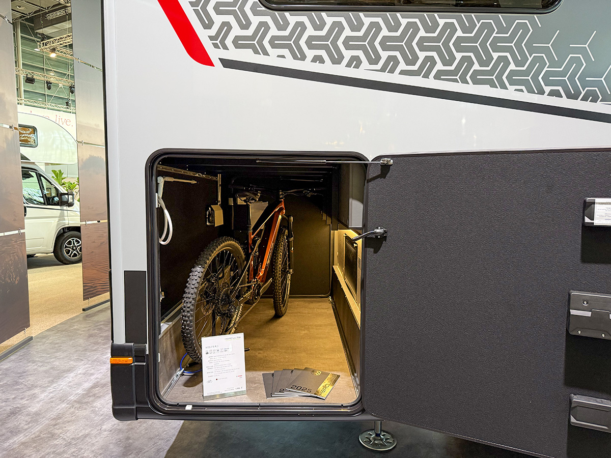 Dethleffs Graneo motorhome garage storage with mountain bike and open rear access door at trade show