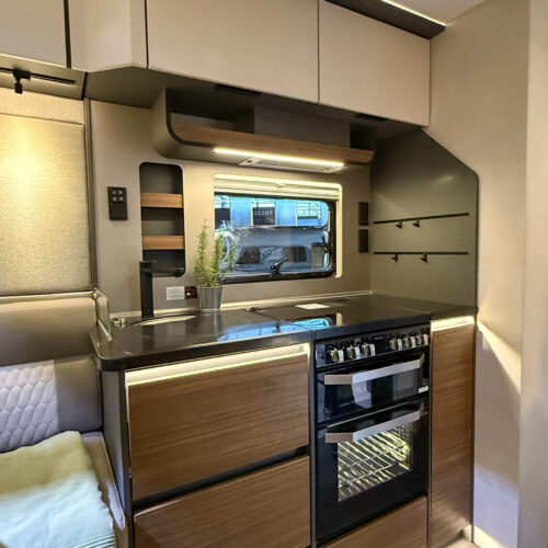 Compact kitchen in the Dethleffs Graneo with sink, hob, dual oven and wood-effect cabinetry beside seating area.