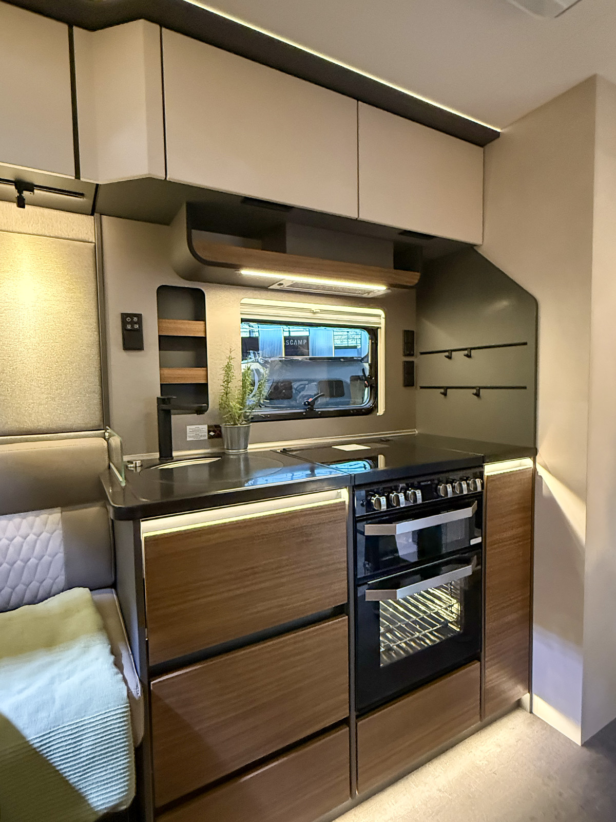 Compact kitchen in the Dethleffs Graneo with sink, hob, dual oven and wood-effect cabinetry beside seating area.