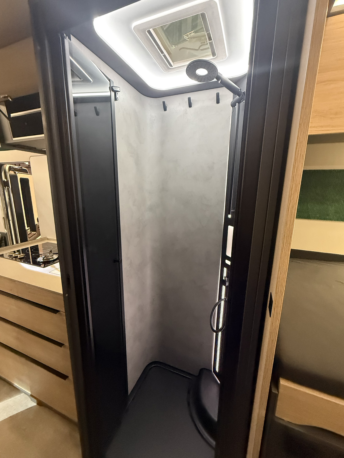 Compact shower cubicle in the Frankia Noctra Liner, featuring skylight, rain showerhead and grey stone-effect walls.