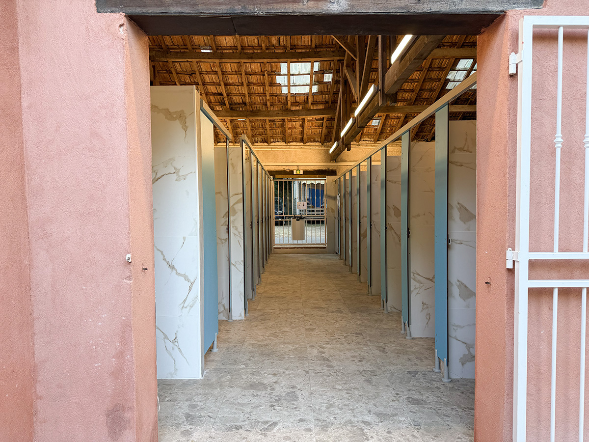 Shower block corridor with marble-effect cubicles at Camping Parc Bellevue Cannes, under a wooden beamed roof