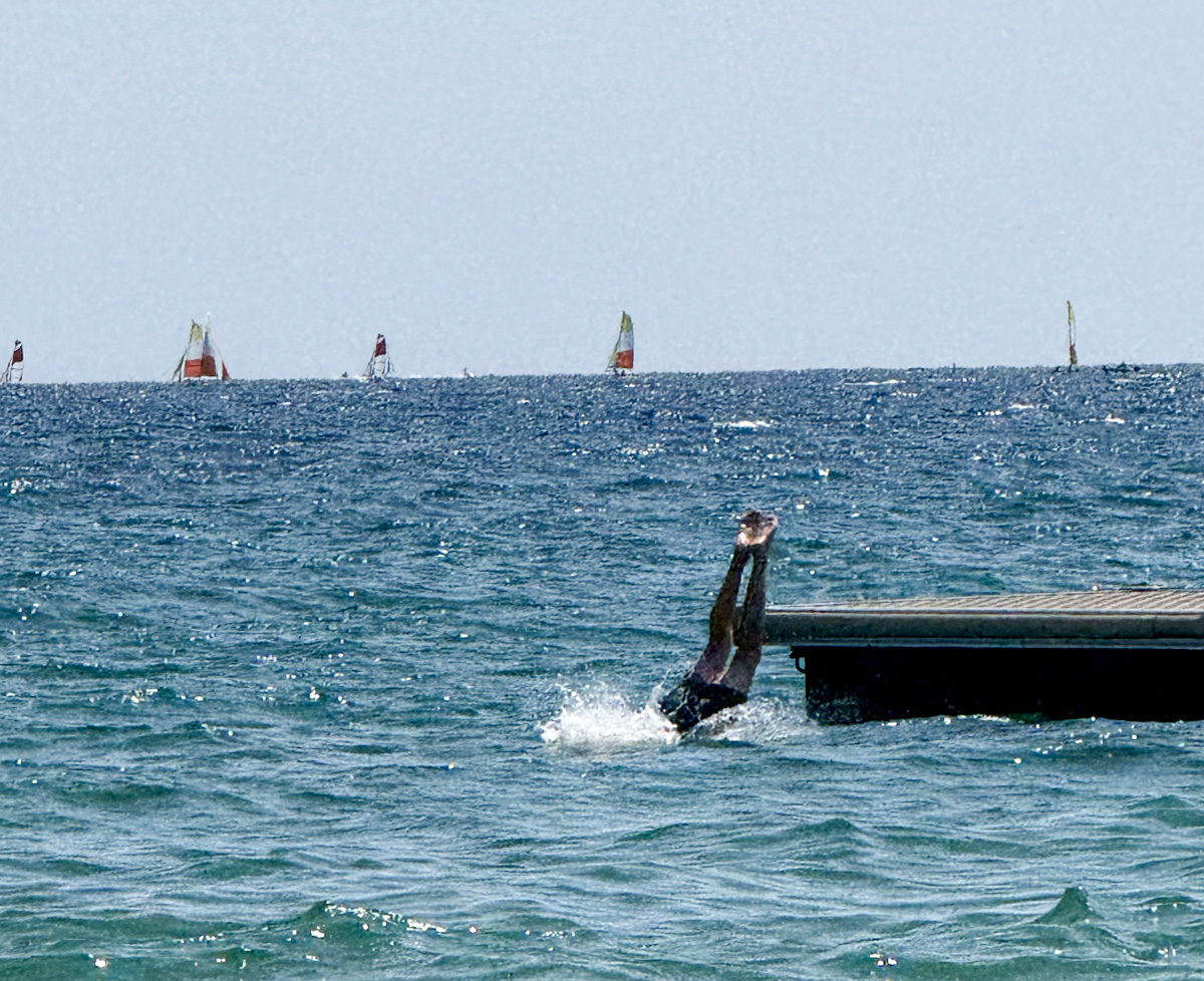 Person diving off jetty into sea near Camping Parc Bellevue Cannes, with sailing boats visible on horizon