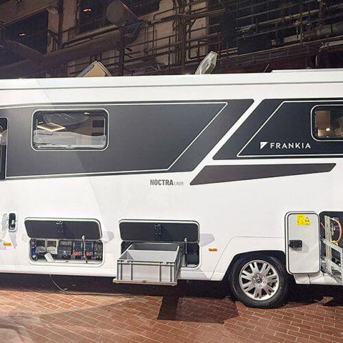 Side view of the Frankia Noctra Liner A-class motorhome showing open storage compartments and sleek black-white exterior design.