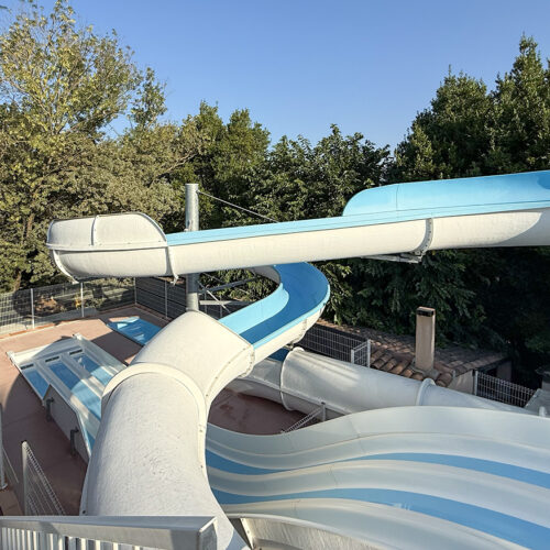 Water slides with blue and white tubes at Camping Parc Bellevue Cannes, overlooking pools and trees.