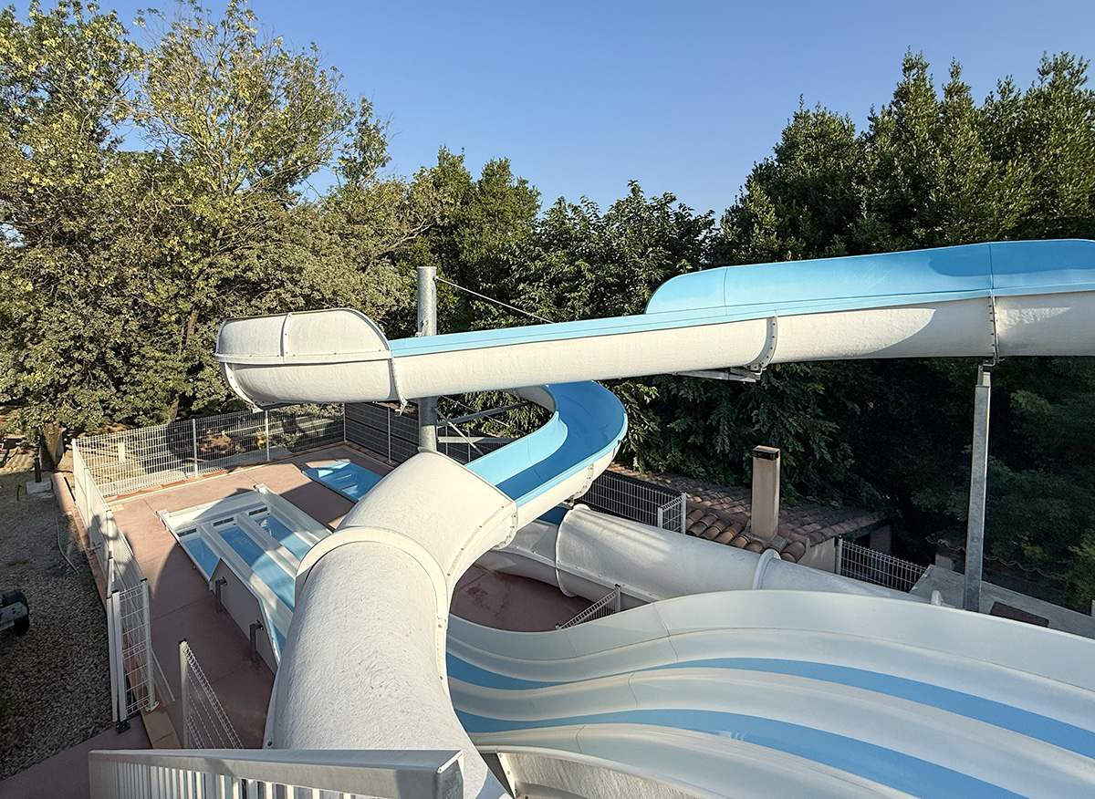 Water slides with blue and white tubes at Camping Parc Bellevue Cannes, overlooking pools and trees.