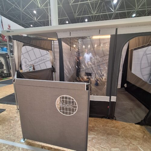 Isabella windscreen accessory displayed at trade show alongside cassette awning tent with clear panel windows