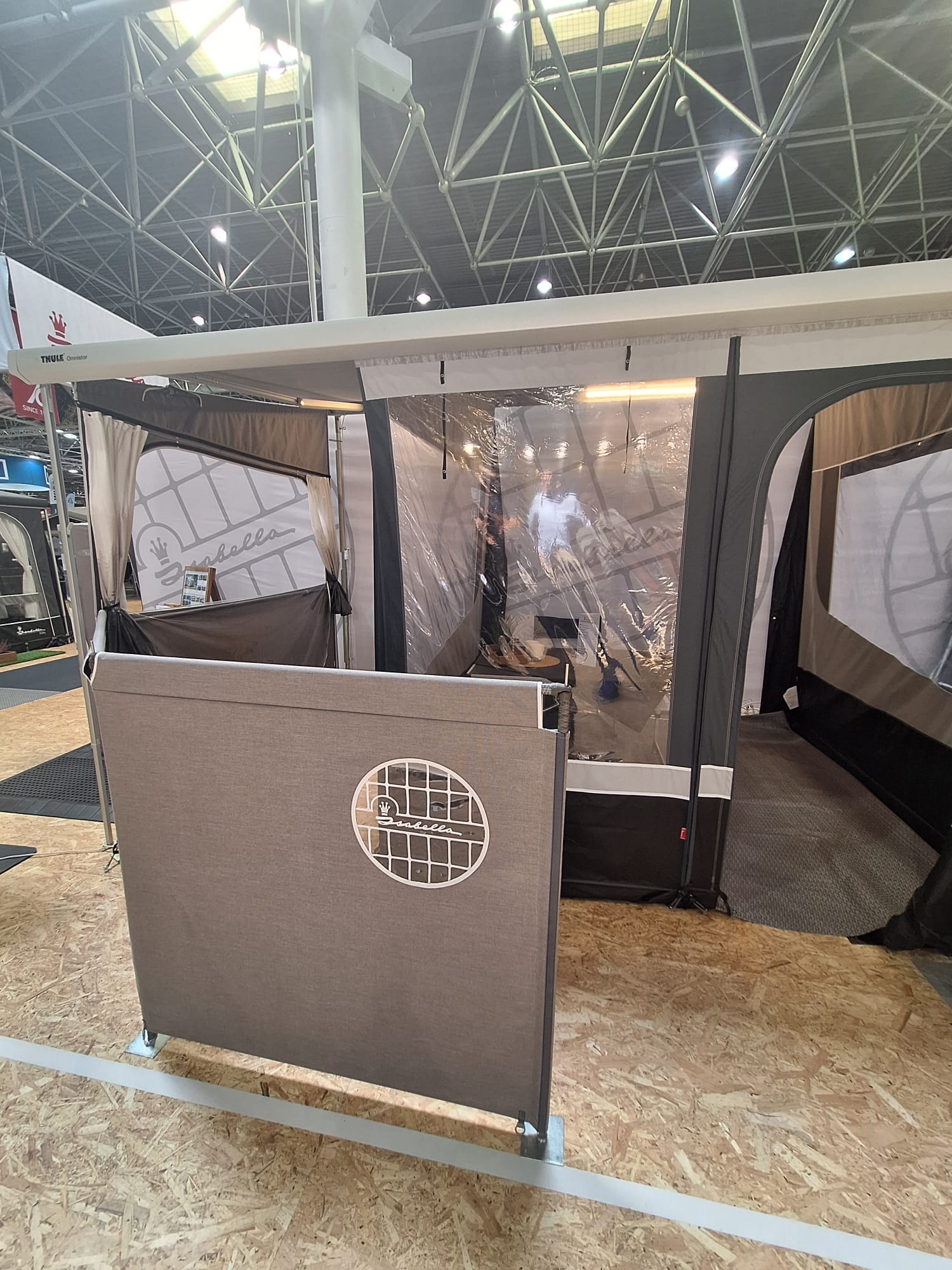 Isabella windscreen accessory displayed at trade show alongside cassette awning tent with clear panel windows