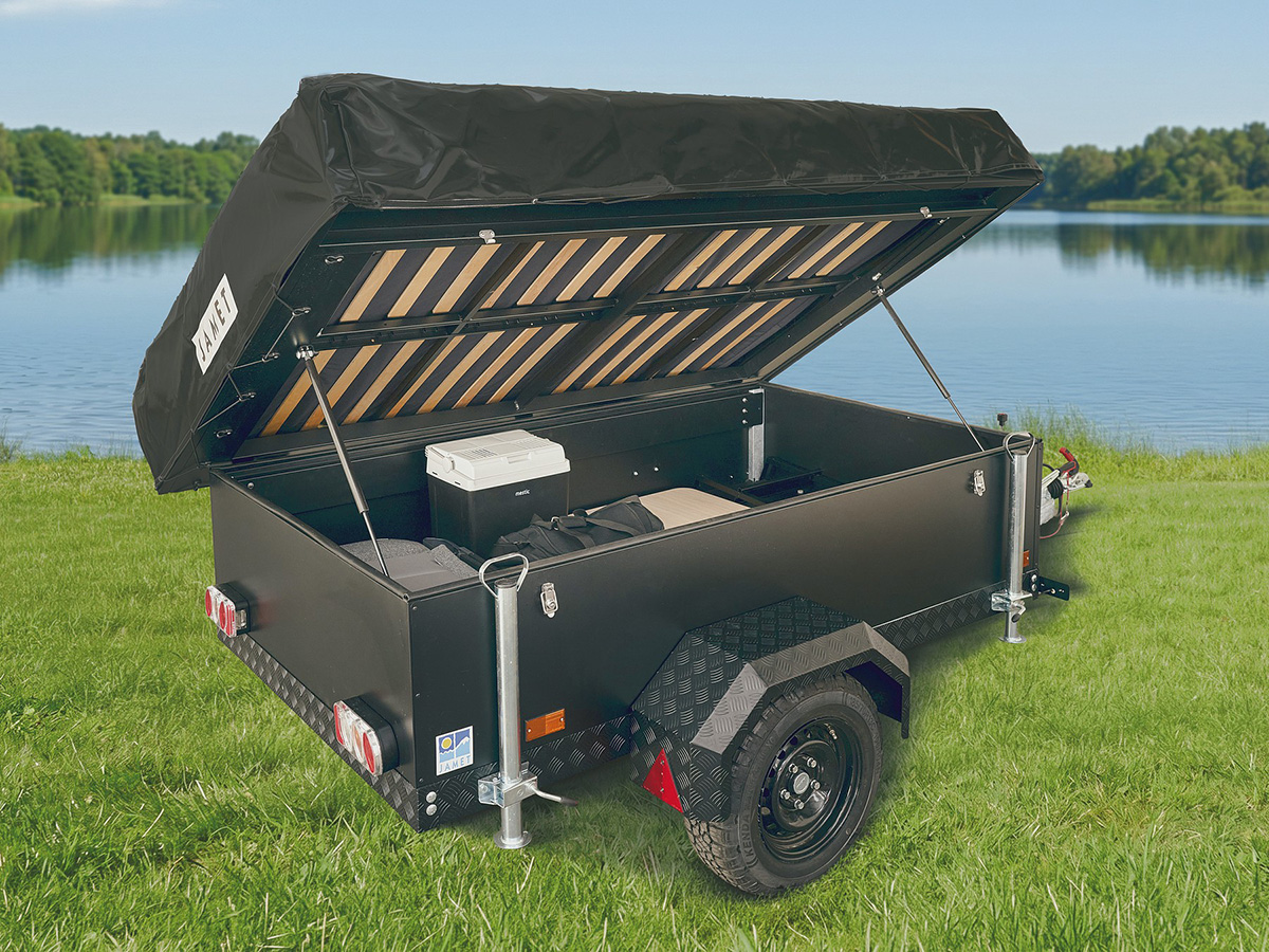 Jamet Offtrail folding trailer with open lid showing storage compartment, cool box and all-terrain tyres by a lake