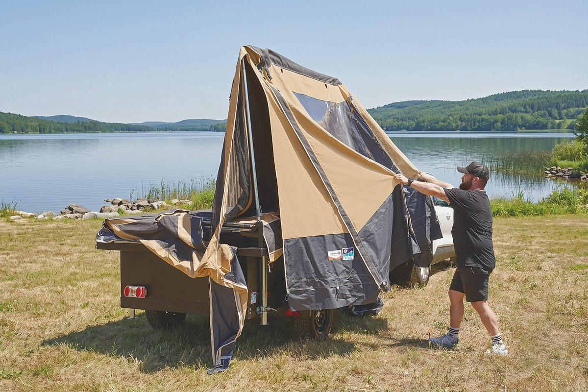 Man setting up Jamet Offtrail folding trailer tent beside a lake, with all-terrain tyres visible
