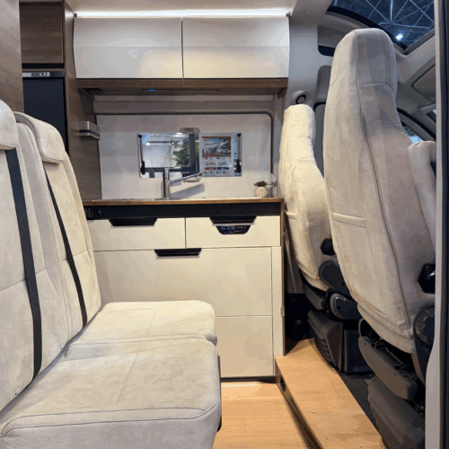 Rapido V64 camper van interior showing dinette seating, kitchenette and swivelled cab seats with wooden flooring