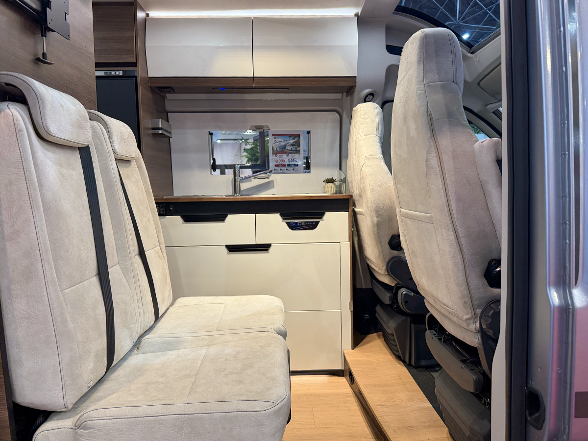 Rapido V64 camper van interior showing dinette seating, kitchenette and swivelled cab seats with wooden flooring